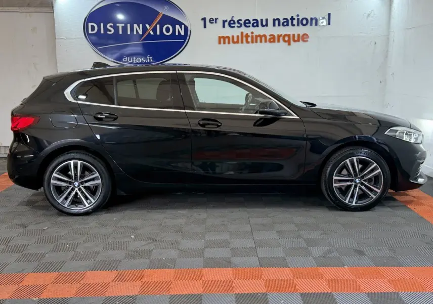 BMW Série 1 116d Business Design noire vue de profil côté gauche, avec jantes alliage et feux arrière allumés.