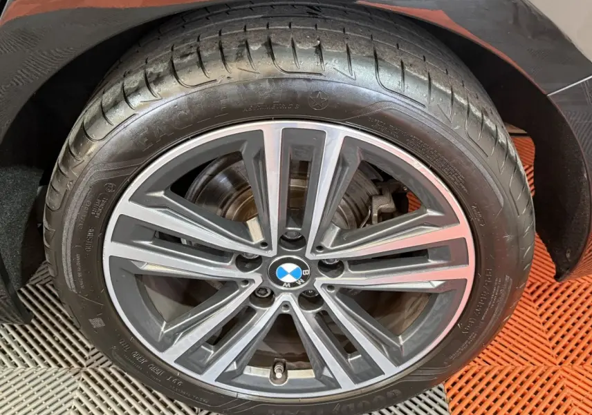 Gros plan sur la roue avant droite d'une BMW Série 1 noire avec jante alliage à dix branches.