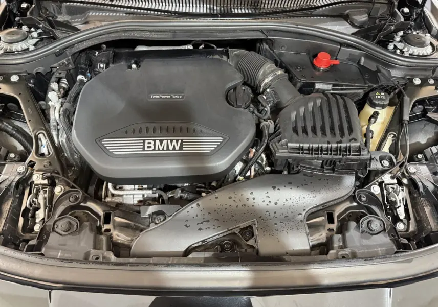 Vue plongeante sur le moteur TwinPower Turbo d'une BMW Série 1 116d noire, avec capot ouvert et détails mécaniques visibles.