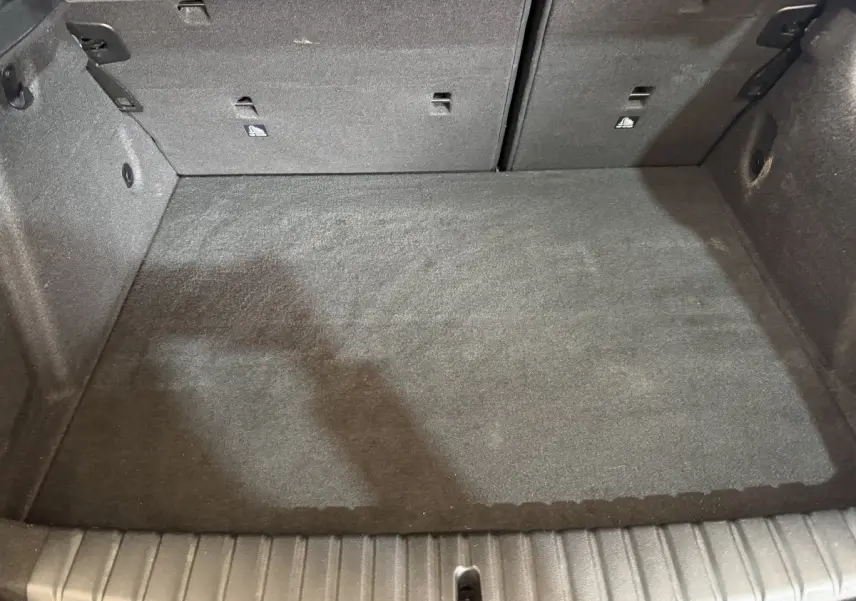 Vue intérieure du coffre noir d'une BMW Série 1 116d DKG7 Business Design, montrant l'espace de chargement avec banquette rabattable.