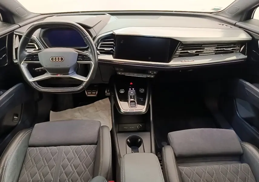 Vue intérieure avant de l'Audi Q4 E-TRON Sportback 2023, tableau de bord noir avec écran tactile et volant multifonctions.