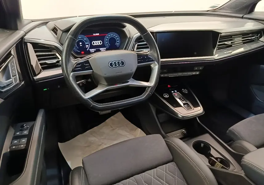 Vue intérieure avant de l'Audi Q4 E-TRON Sportback 2023, tableau de bord noir avec écran tactile et volant multifonctions.