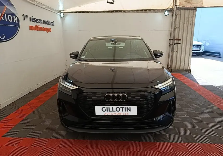Vue avant d'un Audi Q4 E-Tron Sportback noir, avec calandre noire et phares LED dans un showroom.