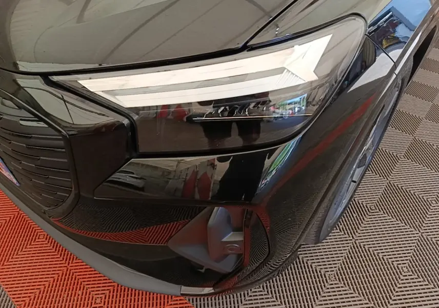 Gros plan sur le phare avant droit noir brillant de l’Audi Q4 E-Tron Sportback 2023 avec calandre et capot visibles.