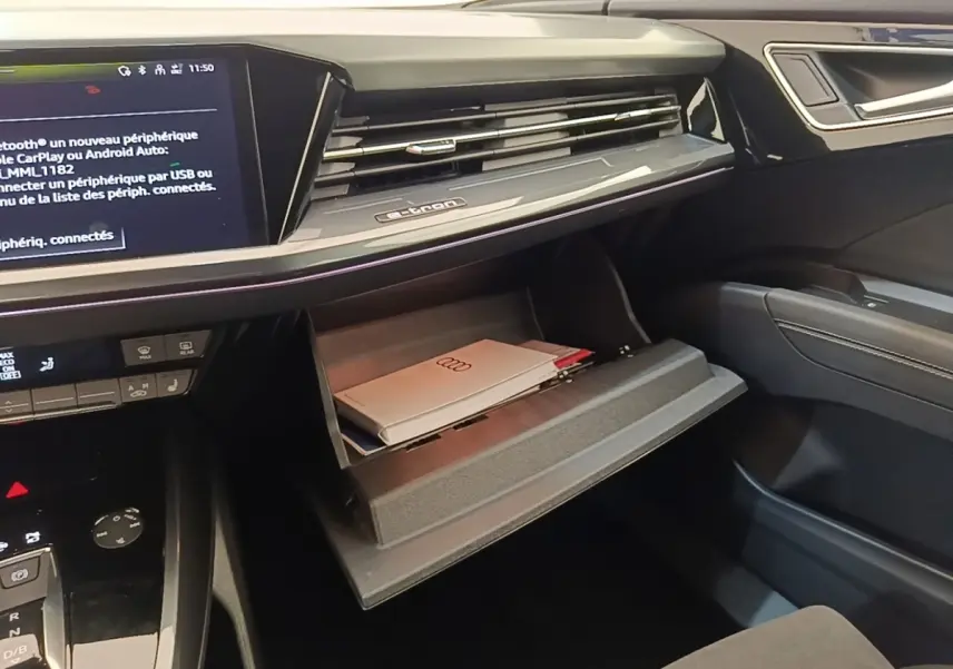 Intérieur noir de l'Audi Q4 E-Tron Sportback 2023, vue sur la boîte à gants ouverte avec documents et écran tactile central.
