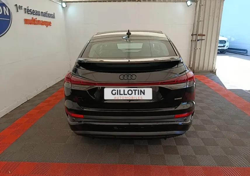 Vue arrière de l'Audi Q4 E-TRON Sportback noir, avec feux LED reliés et spoiler de toit, en intérieur showroom.