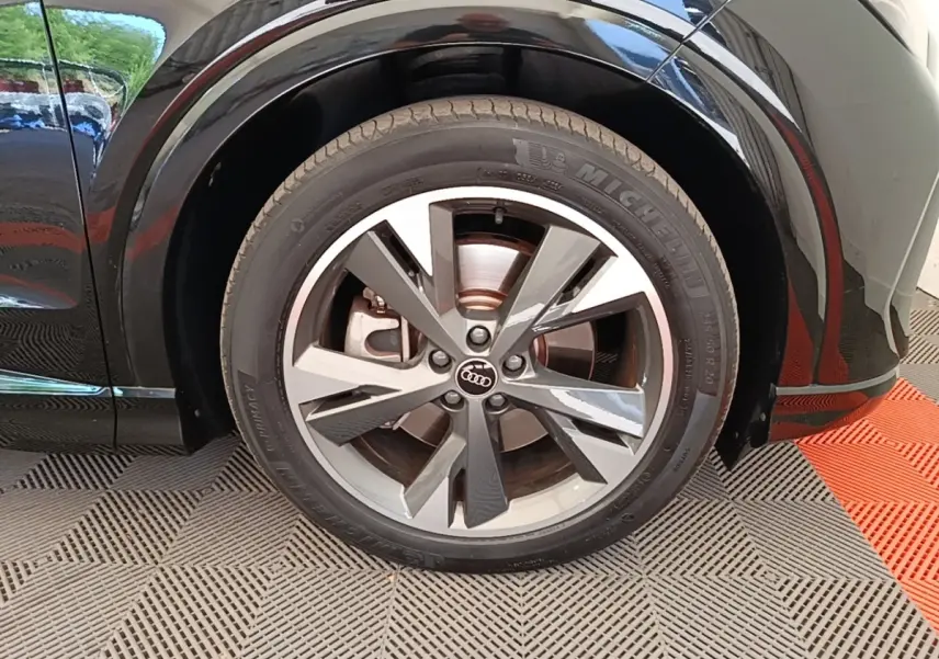 Gros plan sur la roue avant droite noire d’un Audi Q4 E-TRON Sportback électrique avec jante alliage bicolore.