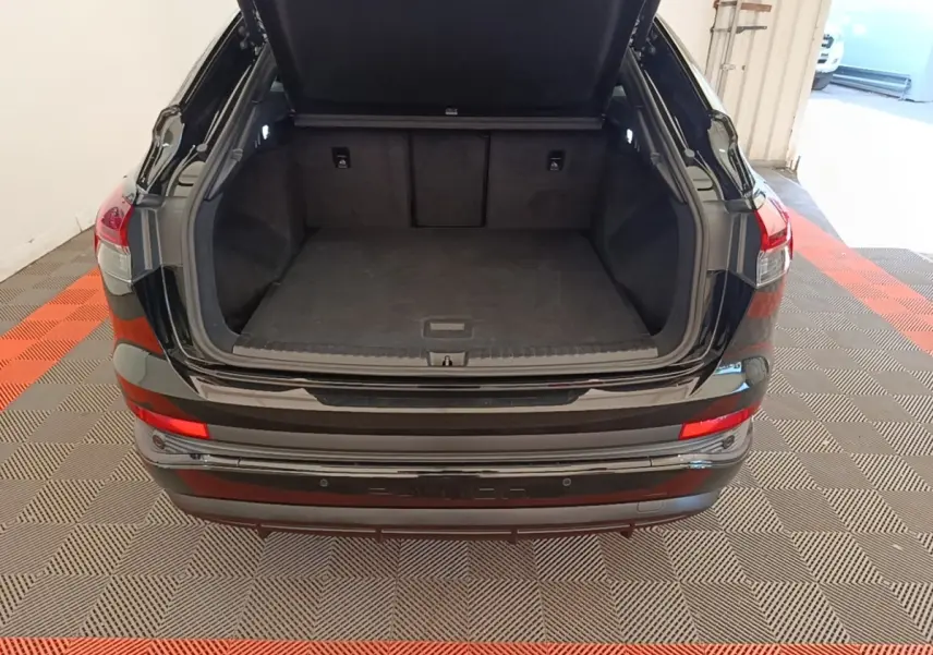 Coffre ouvert vu de l'arrière d'un Audi Q4 E-TRON Sportback noir, montrant l'espace de chargement vide et les feux arrière.
