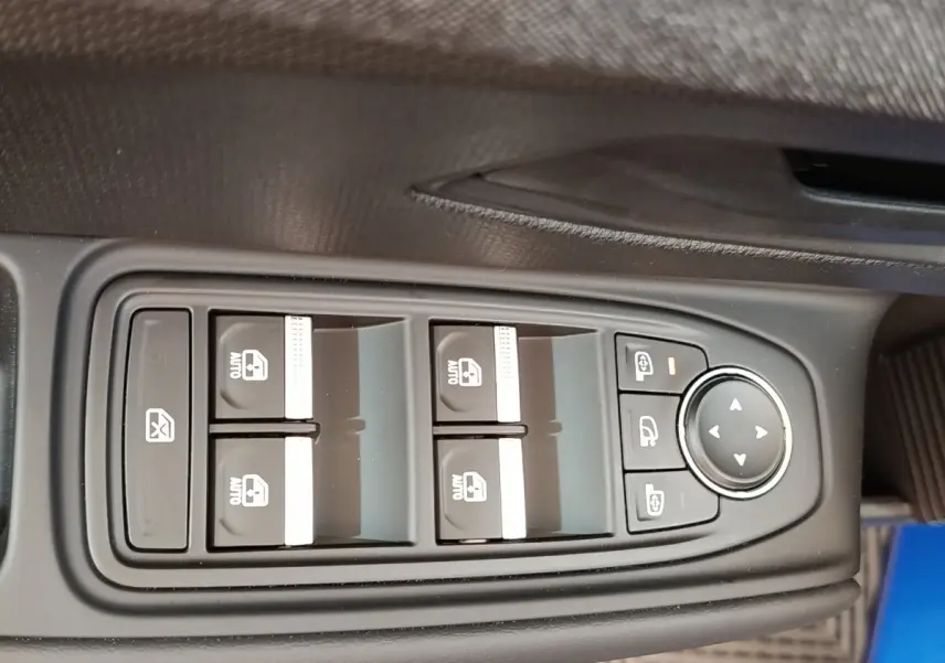 Gros plan sur les commandes des vitres électriques et rétroviseurs d'une Renault Clio bleu, côté conducteur.