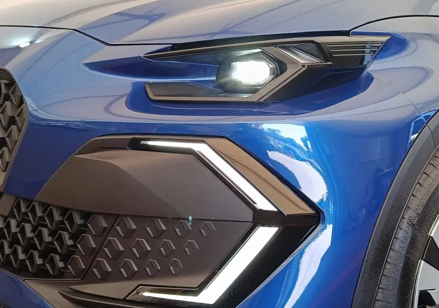 Gros plan sur le phare avant droit allumé de la Renault Clio Evolution TCe 115 bleu brillant avec signature lumineuse en forme de flèche.