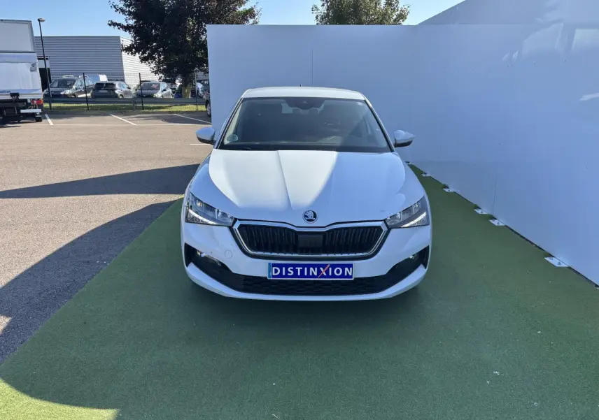 Vue frontale d'une Skoda Scala blanc glacier avec calandre noire et plaque Distinxion sur fond extérieur.