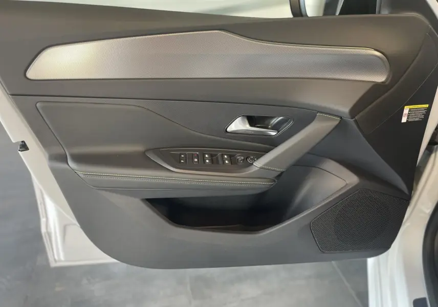 Porte avant gauche ouverte d'une Peugeot 308 blanche, intérieur noir avec surpiqûres vertes et commandes électriques.