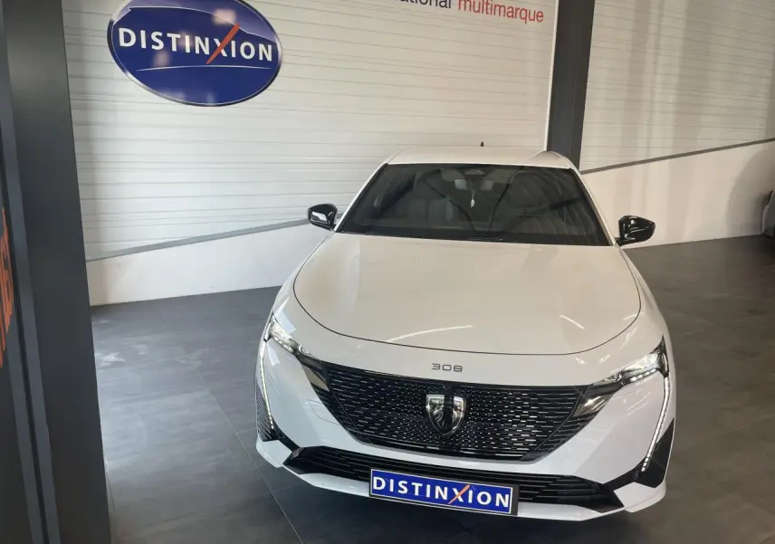 Peugeot 308 blanche vue de face, avec calandre noire brillante et feux LED distinctifs en intérieur showroom.