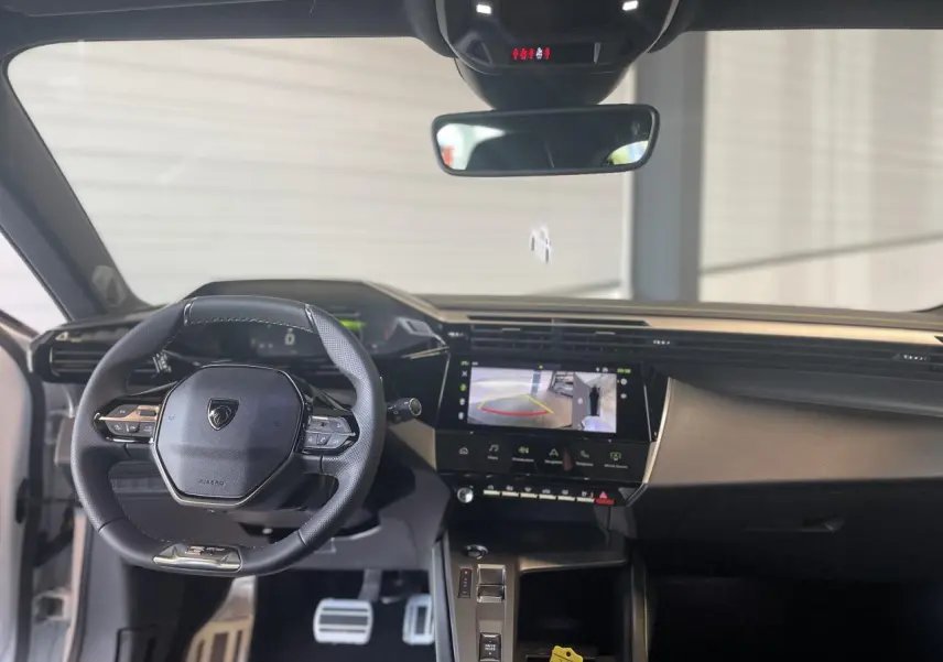 Intérieur avant de la Peugeot 308 2025, vue du poste de conduite avec volant compact et écran tactile affichant la caméra de recul.