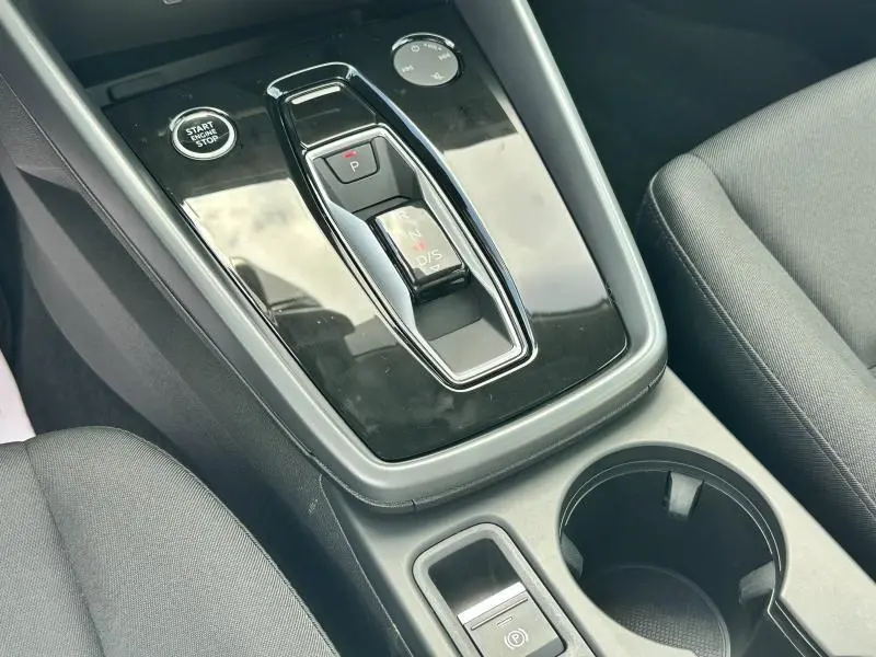 Vue rapprochée de la console centrale noire brillante avec levier de boîte auto et bouton Start/Stop de l'Audi A3 Sportback blanche Arkona.