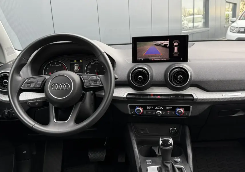 Vue intérieure de l'Audi Q2 35 TFSI 150 S-Tronic S-Line 2023, tableau de bord avec écran caméra de recul et volant cuir noir.