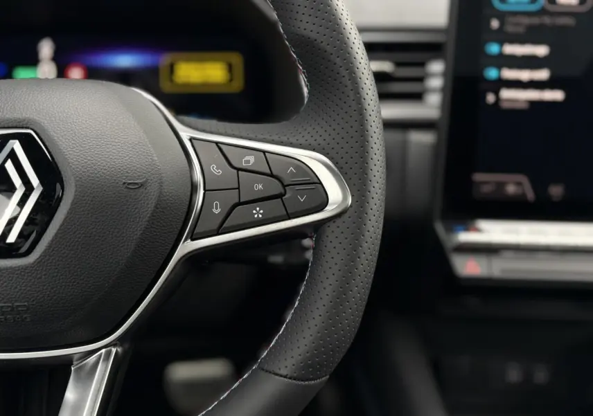 Gros plan sur le volant perforé noir avec commandes multifonctions et logo Renault du Captur E-Tech Full Hybrid 2025.
