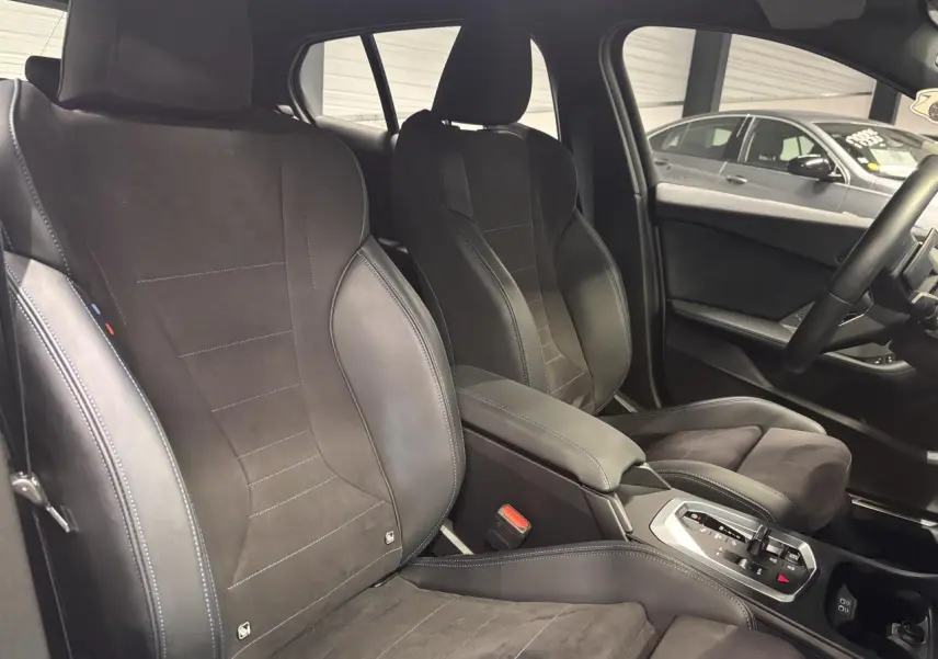 Vue intérieure des sièges avant en Alcantara noir avec surpiqûres bleues et console centrale d’une BMW Série 1 M Sport.