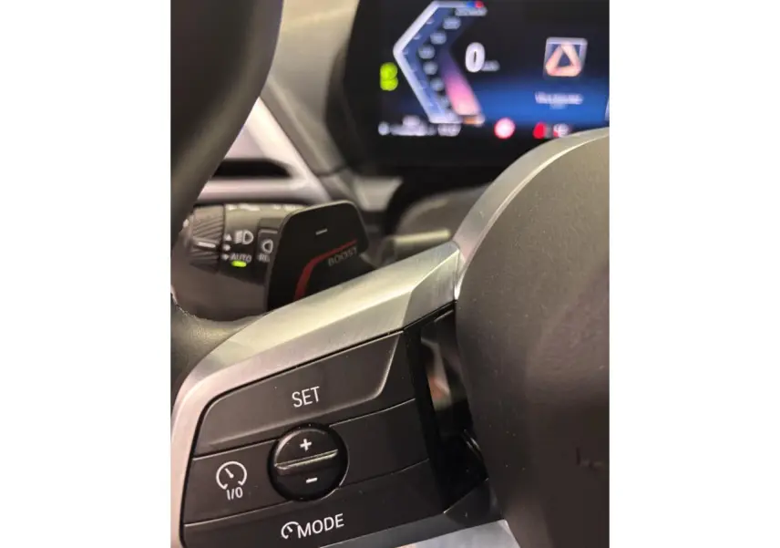 Gros plan sur les commandes au volant côté gauche de la BMW Série 1 118d M Sport, avec affichage numérique flou en arrière-plan.