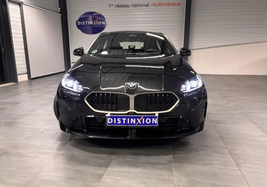 BMW Série 1 118d M Sport noir métal vue de face avec calandre chromée et phares LED allumés dans un showroom.