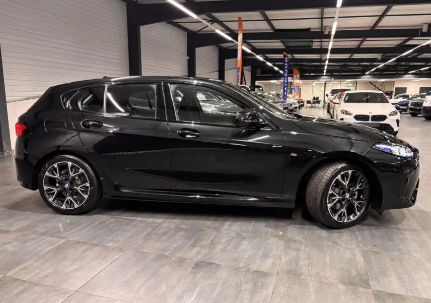 BMW Série 1 118d M Sport noir métal vue de profil côté gauche avec jantes alliage 18 pouces en intérieur showroom.