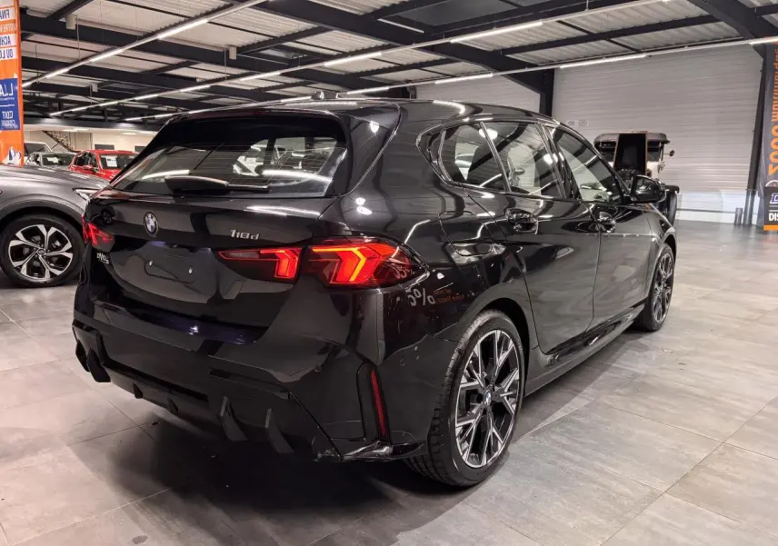 BMW Série 1 118d noire métal vue 3/4 arrière droit en intérieur avec jantes alliage 18 pouces M Sport.