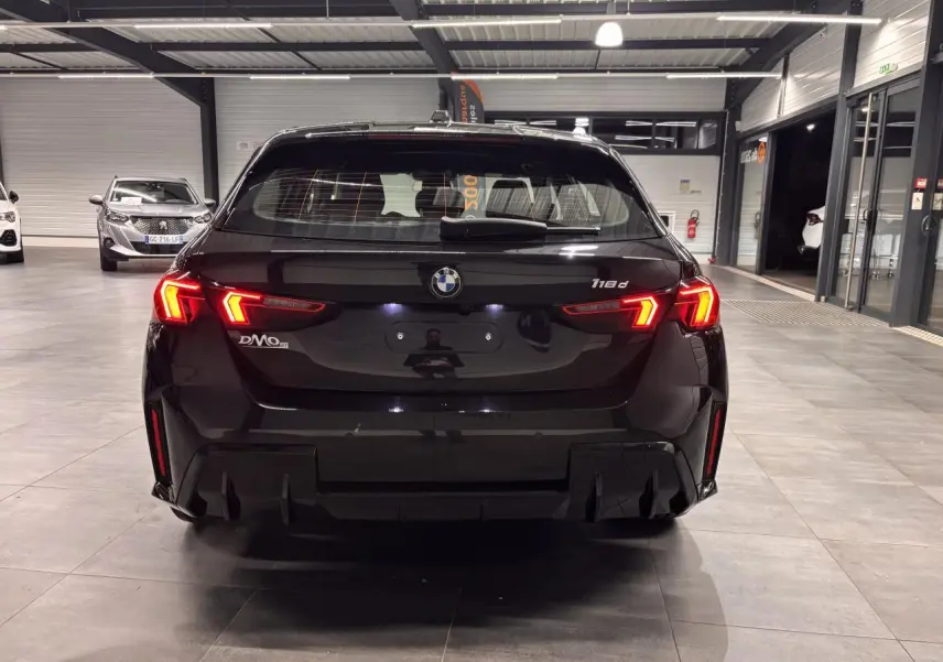 Vue arrière d'une BMW Série 1 118d noire métal avec feux arrière LED allumés dans un showroom.