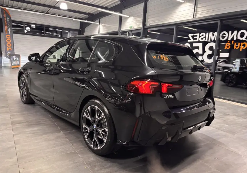 BMW Série 1 118d M Sport noir métal vue 3/4 arrière droit en intérieur avec jantes 18 pouces bicolores et feux LED.