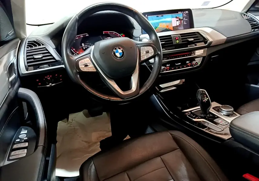 Vue intérieure côté conducteur du BMW X3 noir 2019, volant cuir, écran tactile central et console moderne.