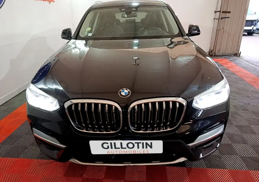 Vue avant d'un BMW X3 sDrive18d noir avec calandre double haricot et phares LED allumés en intérieur showroom.