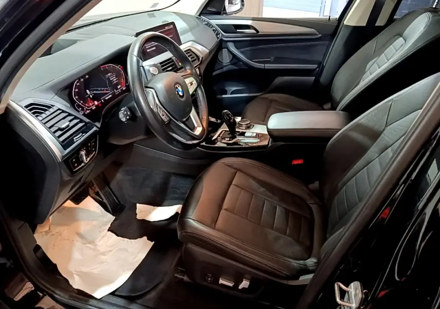 Vue intérieure côté conducteur du BMW X3 noir 2019, avec tableau de bord digital et sièges cuir noirs.