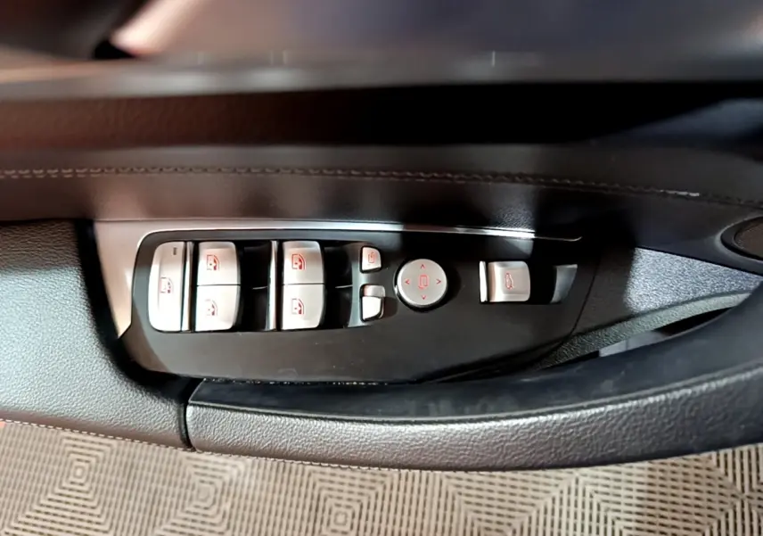 Gros plan sur les commandes des lève-vitres et rétroviseurs côté conducteur d’une BMW X3 noir 2019.