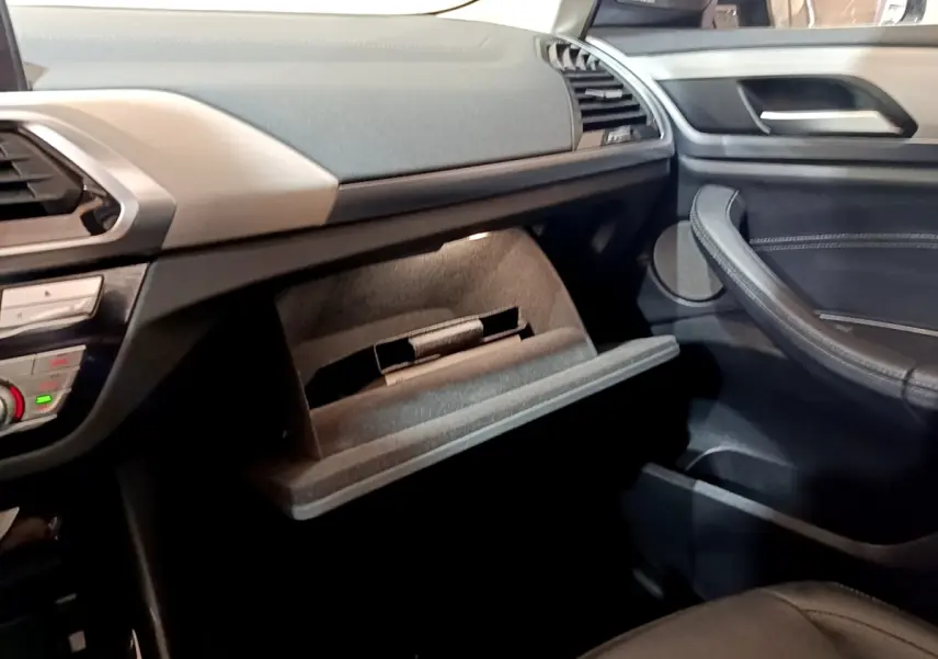 Intérieur BMW X3 sDrive18d 2019, vue côté passager sur boîte à gants ouverte et tableau de bord noir et beige.