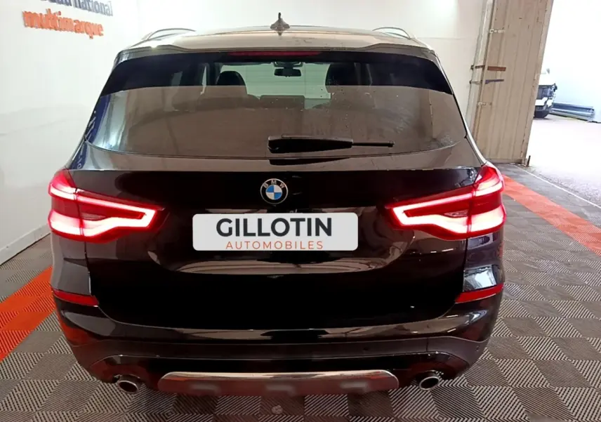 Vue arrière d'un BMW X3 noir avec feux arrière allumés dans un garage intérieur.