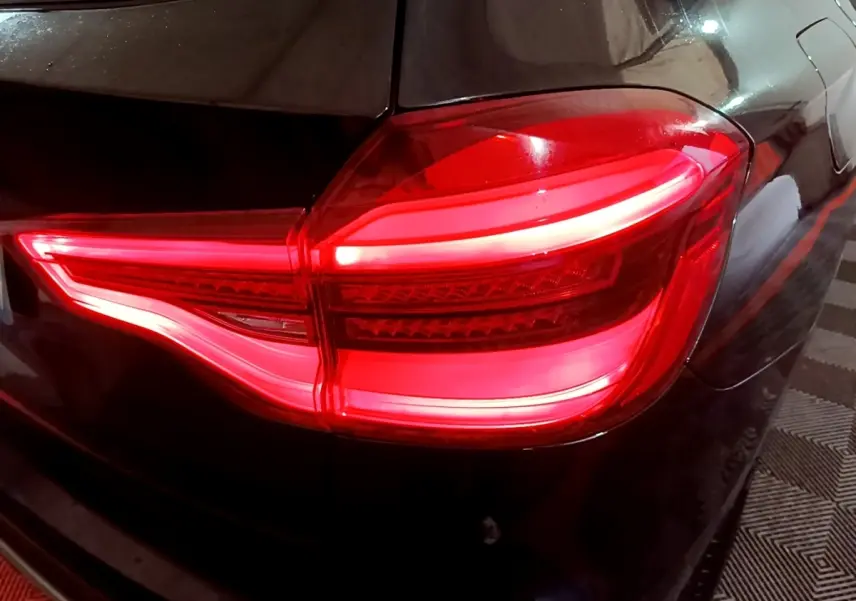 Gros plan sur le feu arrière droit allumé d’un BMW X3 noir, soulignant les lignes lumineuses LED distinctives.