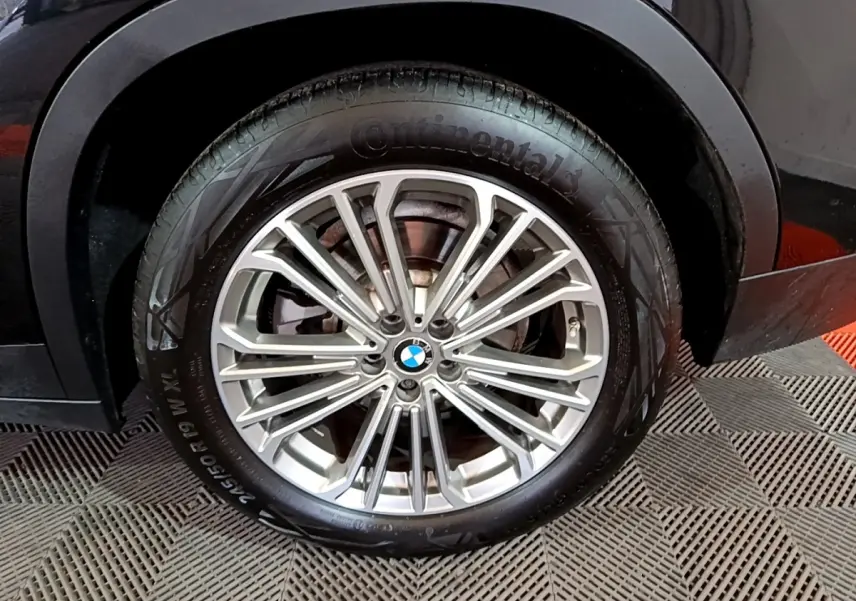 Gros plan sur la roue avant droite d’un BMW X3 noir, mettant en valeur la jante alliage multi-branches argentée.