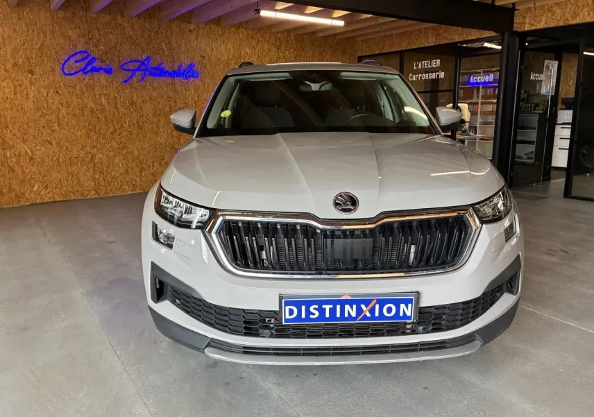 Vue frontale d'un Skoda Kodiaq gris clair 2023 en showroom, avec calandre noire et logo distinctif au centre.