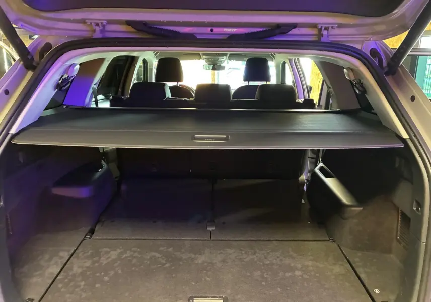 Vue arrière du coffre ouvert d'un Skoda Kodiaq gris clair 2023, avec cache-bagages déployé et sièges arrière visibles.