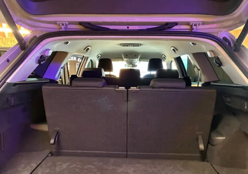 Vue arrière intérieure du coffre ouvert d’un Skoda Kodiaq gris clair 2023, montrant la troisième rangée de sièges en tissu noir relevée.