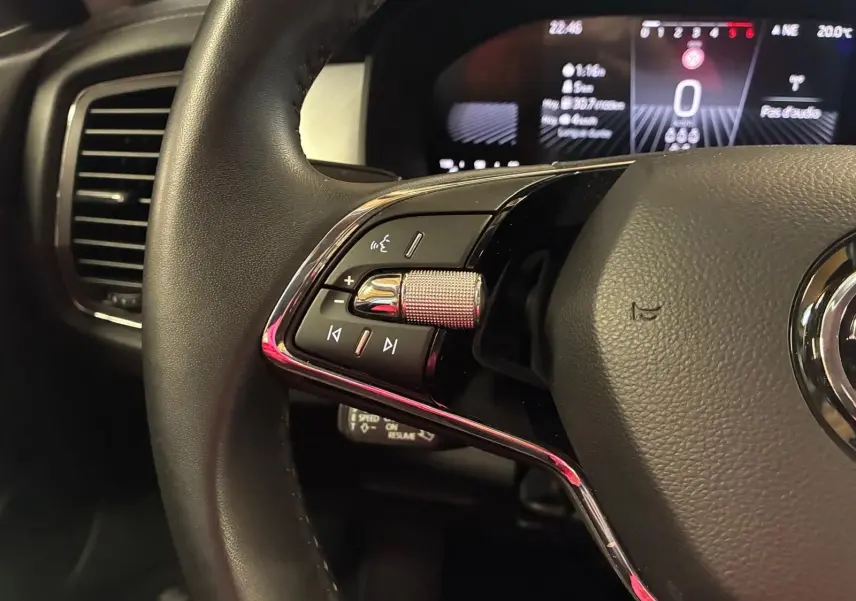 Gros plan sur la partie gauche du volant noir du Skoda Kodiaq gris clair 2023, avec commandes audio et tableau de bord numérique en arrière-plan.