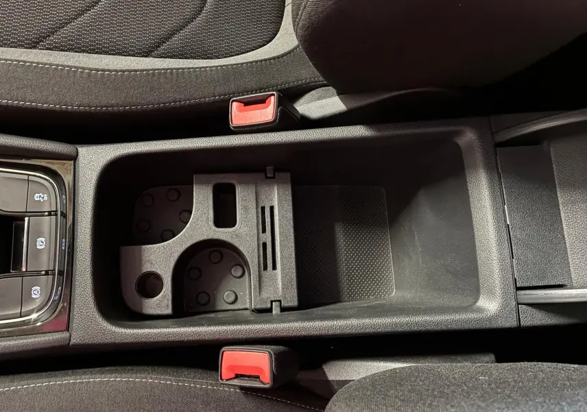 Vue rapprochée de la console centrale noire du Skoda Kodiaq 2023, montrant porte-gobelets et accoudoir entre sièges tissu.