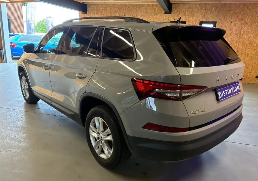 Vue 3/4 arrière droite d'un Skoda Kodiaq gris clair 2023 avec feux arrière LED et vitres teintées en intérieur d'atelier.