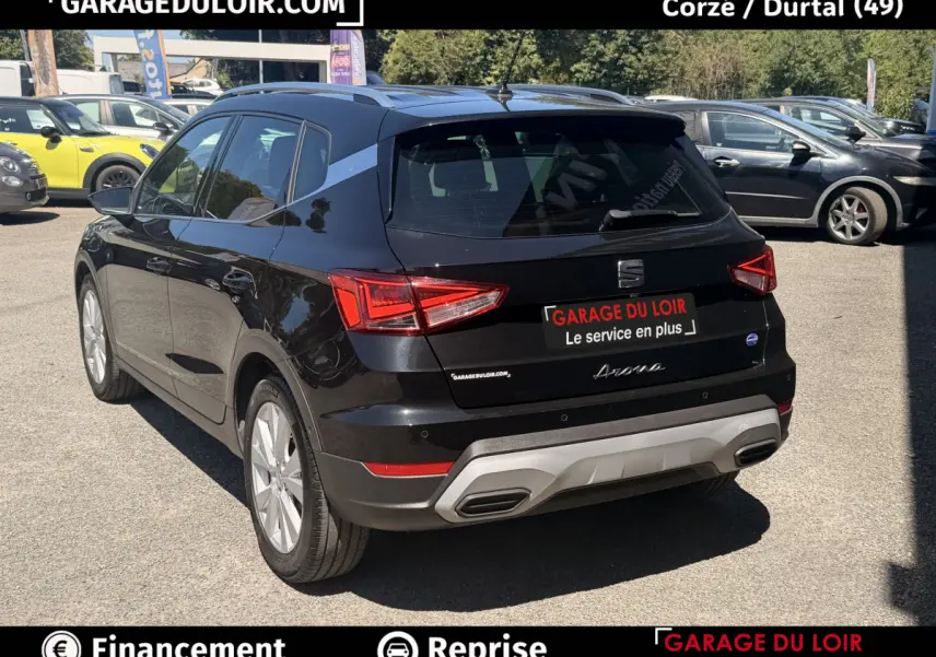 Vue 3/4 arrière droite d'une SEAT Arona noire 2025 avec jantes alliage et barres de toit chromées sur parking.