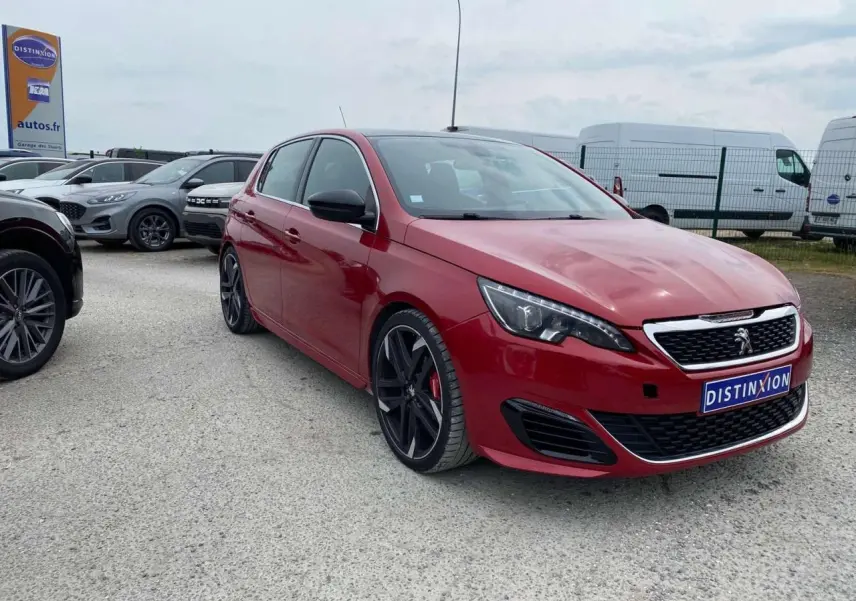Peugeot 308 GTi rouge vue 3/4 avant avec jantes noires et calandre chromée sur parking extérieur.