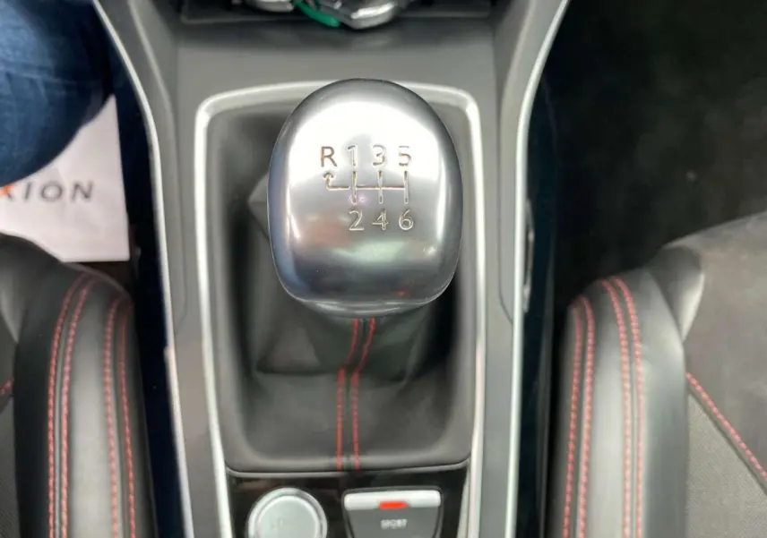 Le levier de vitesses manuel en aluminium de la Peugeot 308 GTi rouge, avec coutures rouges visibles sur la console.