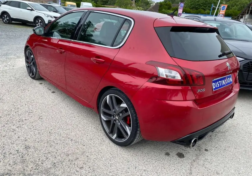 Vue 3/4 arrière droite d'une Peugeot 308 GTi rouge métallisée avec jantes sport et double sortie d'échappement.