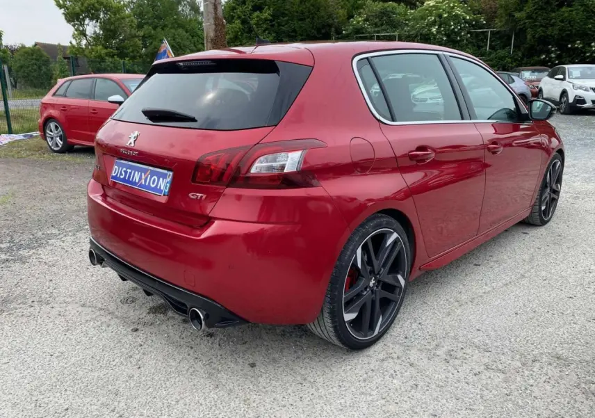 Peugeot 308 GTi rouge vue 3/4 arrière droit, avec jantes noires et double sortie d'échappement chromée.