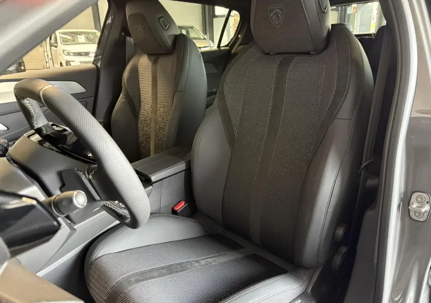 Vue intérieure côté conducteur de la Peugeot 308 gris selenium, sièges en cuir et tissu avec logo Peugeot brodé sur appuie-tête.