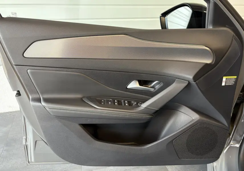 Porte avant gauche ouverte d'une Peugeot 308 gris selenium, montrant le panneau de porte avec commandes et finition noire élégante.