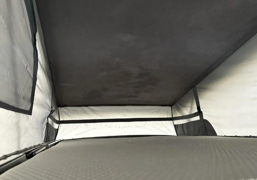 Intérieur du toit relevable du Volkswagen Transporter jaune et blanc, vue en plongée sur la couchette aménagée.